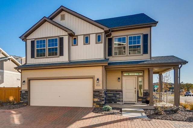 craftsman-style house featuring an attached garage, covered porch, stone siding, decorative driveway, and board and batten siding