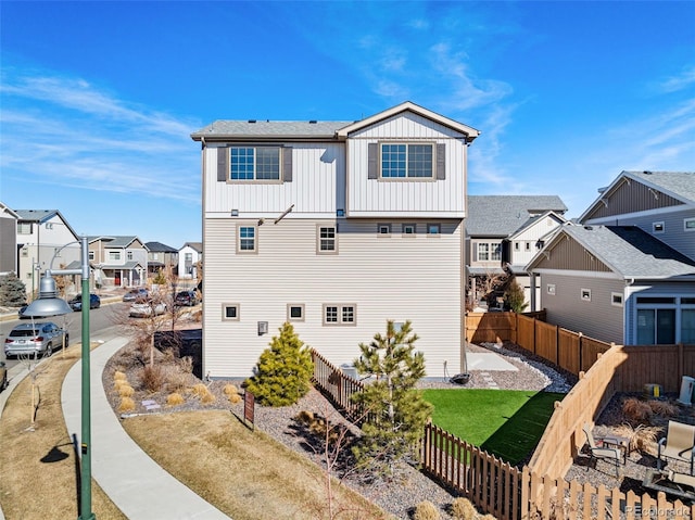 rear view of property with a fenced backyard, a residential view, board and batten siding, and a yard