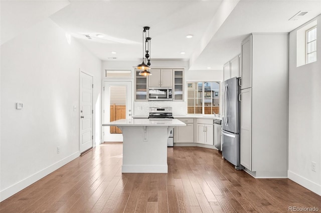 kitchen featuring a center island, decorative light fixtures, light countertops, appliances with stainless steel finishes, and glass insert cabinets