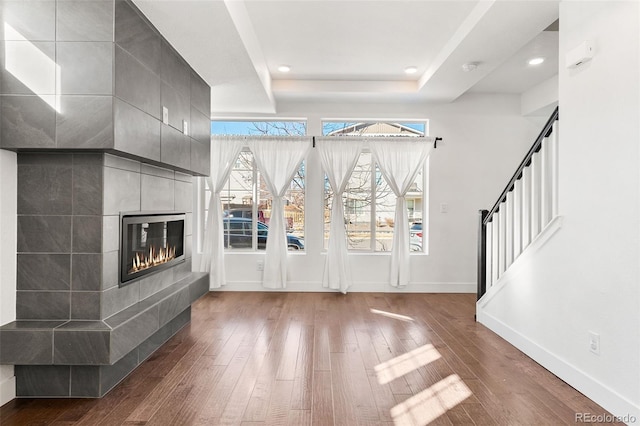 foyer entrance featuring a tray ceiling, a fireplace, wood finished floors, and baseboards