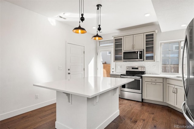 kitchen with dark wood finished floors, glass insert cabinets, appliances with stainless steel finishes, decorative light fixtures, and light countertops