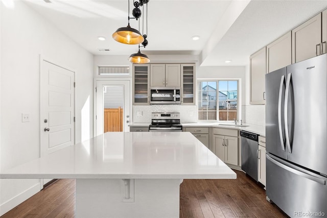 kitchen featuring a center island, light countertops, hanging light fixtures, appliances with stainless steel finishes, and glass insert cabinets