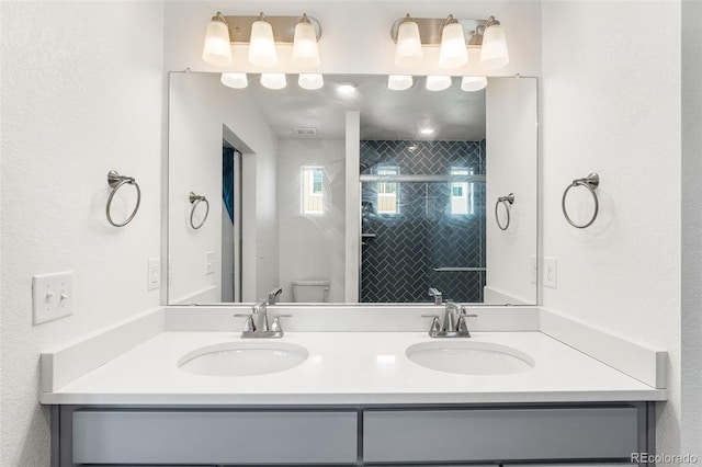 bathroom with double vanity, a stall shower, a sink, and toilet