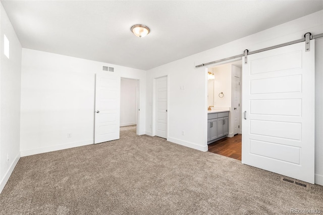 unfurnished bedroom featuring a barn door, visible vents, dark colored carpet, and baseboards