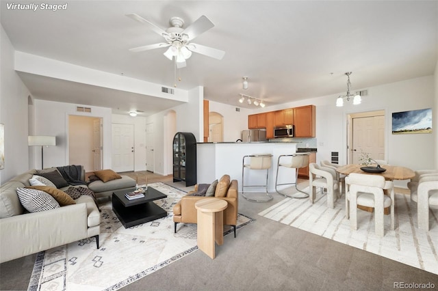 carpeted living room with rail lighting and ceiling fan with notable chandelier