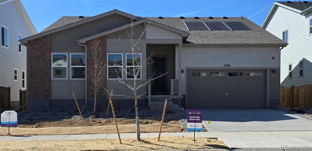 view of front of house featuring fence, driveway, roof with shingles, solar panels, and a garage