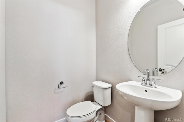 half bathroom with toilet, baseboards, and a sink