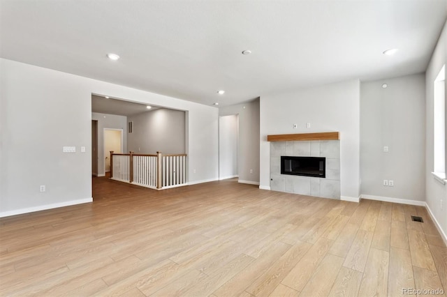 unfurnished living room with light wood finished floors, recessed lighting, a tiled fireplace, and baseboards