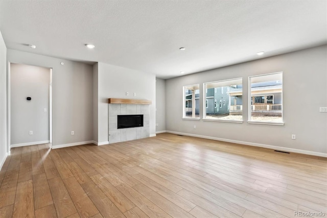 unfurnished living room featuring visible vents, a tiled fireplace, a textured ceiling, wood finished floors, and baseboards