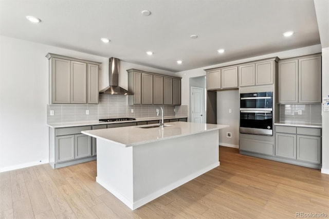 kitchen featuring a sink, appliances with stainless steel finishes, gray cabinetry, and wall chimney range hood