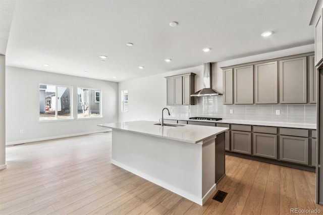 kitchen featuring tasteful backsplash, light wood finished floors, wall chimney range hood, stainless steel gas stovetop, and a sink