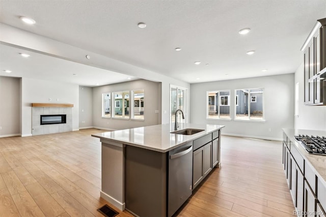 kitchen with visible vents, light wood finished floors, a sink, appliances with stainless steel finishes, and a tiled fireplace