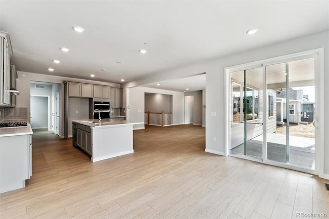 kitchen featuring gas cooktop, open floor plan, recessed lighting, light wood-style floors, and light countertops