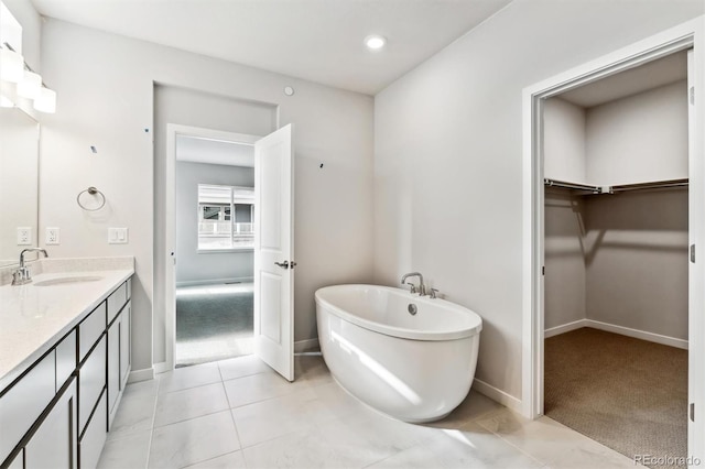 full bath featuring vanity, baseboards, a soaking tub, tile patterned flooring, and a walk in closet