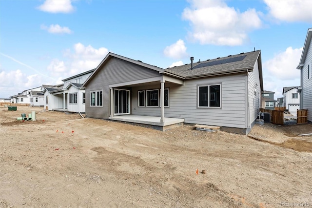 back of property with a patio area, central AC unit, solar panels, and roof with shingles