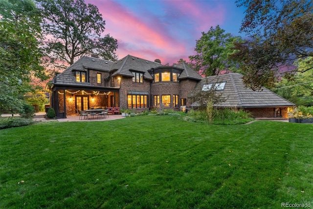 back of house at dusk with a patio area, a chimney, and a yard