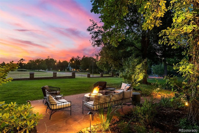 patio terrace at dusk with an outdoor fire pit, a yard, and fence