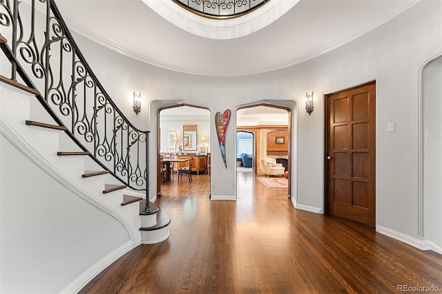 foyer featuring arched walkways, ornamental molding, dark wood-style floors, and baseboards