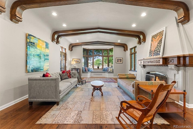 living room featuring lofted ceiling with beams, a lit fireplace, wood finished floors, and baseboards