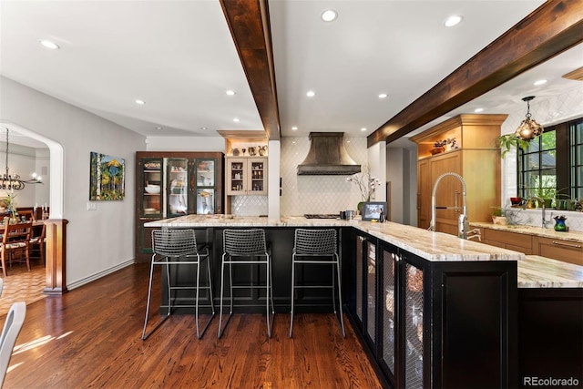 kitchen with light stone counters, dark wood-type flooring, a breakfast bar, beam ceiling, and custom range hood