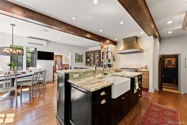 kitchen with a sink, a large island, a wall mounted AC, custom exhaust hood, and dark wood-style floors