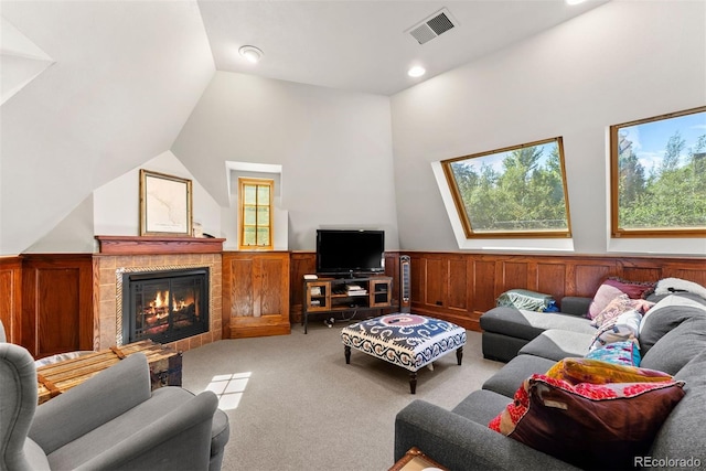 living room with light colored carpet, a fireplace, visible vents, vaulted ceiling, and wainscoting