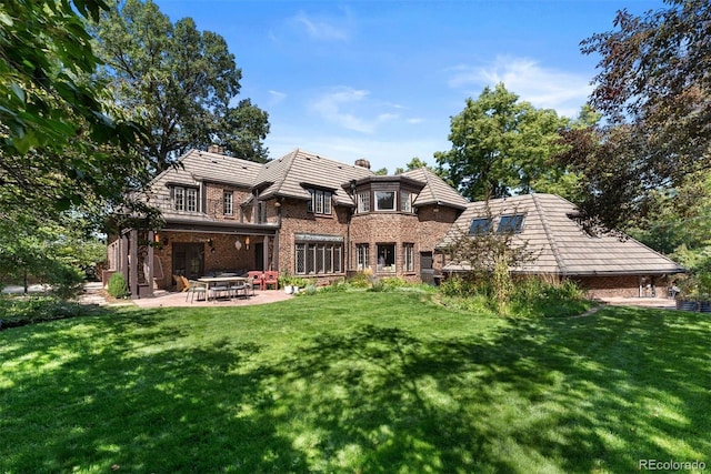 rear view of house with a yard, brick siding, a chimney, and a patio area