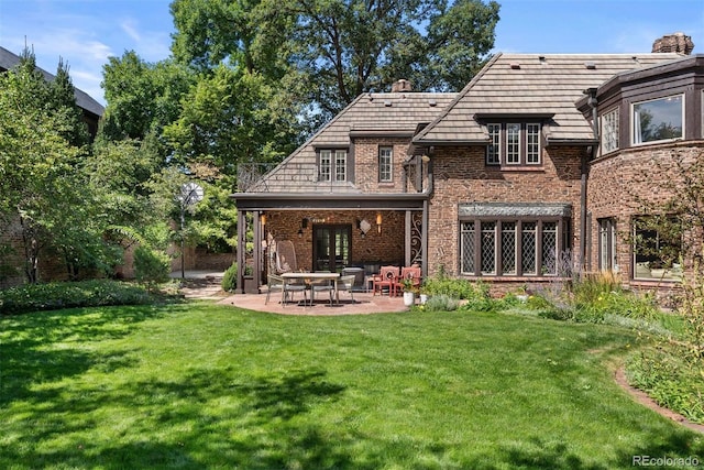 rear view of house with brick siding, a lawn, a chimney, and a patio