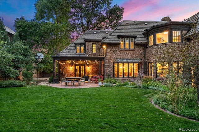 back of property with brick siding, a lawn, a chimney, and a patio