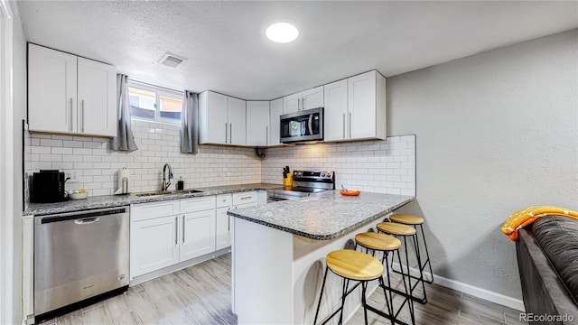 kitchen with appliances with stainless steel finishes, white cabinetry, sink, a kitchen breakfast bar, and kitchen peninsula