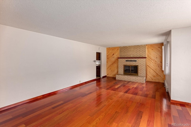 unfurnished living room featuring a fireplace, a textured ceiling, dark hardwood / wood-style floors, and wooden walls