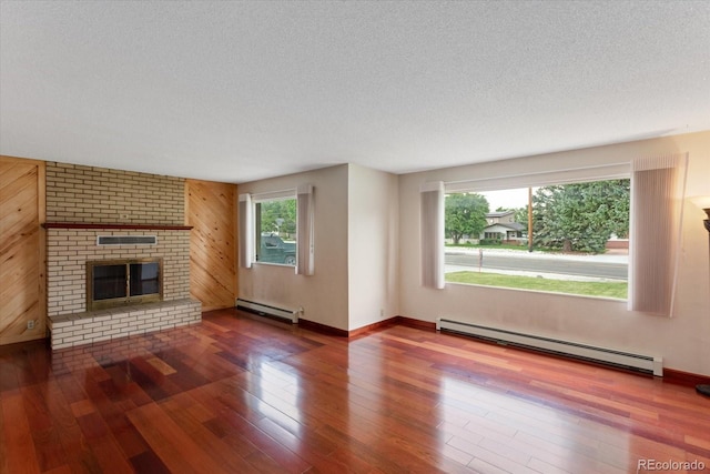 unfurnished living room featuring a brick fireplace, wood walls, a wealth of natural light, and a baseboard heating unit