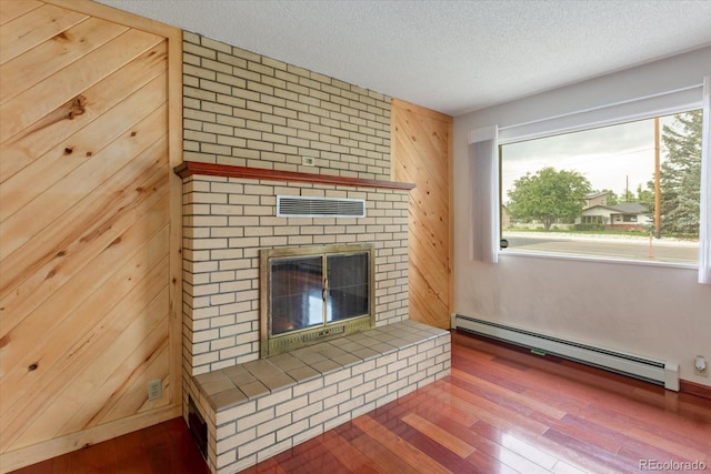 unfurnished living room with a brick fireplace, a textured ceiling, wood-type flooring, a baseboard radiator, and wood walls