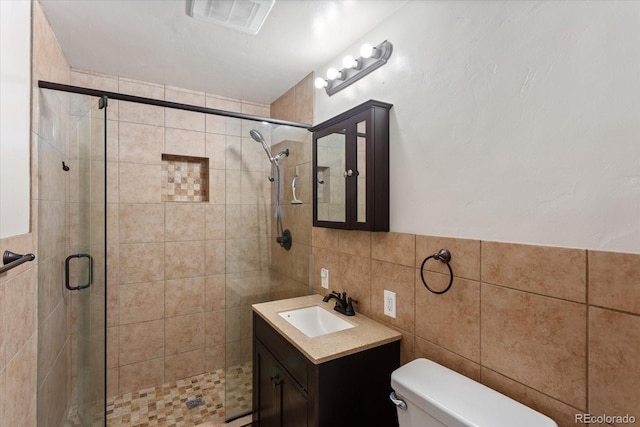 bathroom with vanity, toilet, a shower with shower door, and tile walls