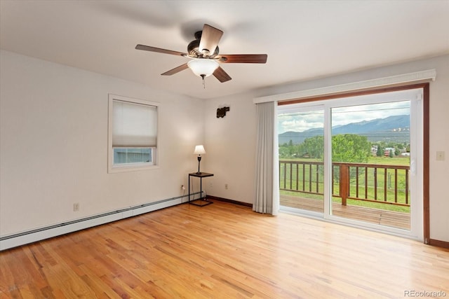 spare room featuring baseboard heating, a mountain view, ceiling fan, and light hardwood / wood-style floors