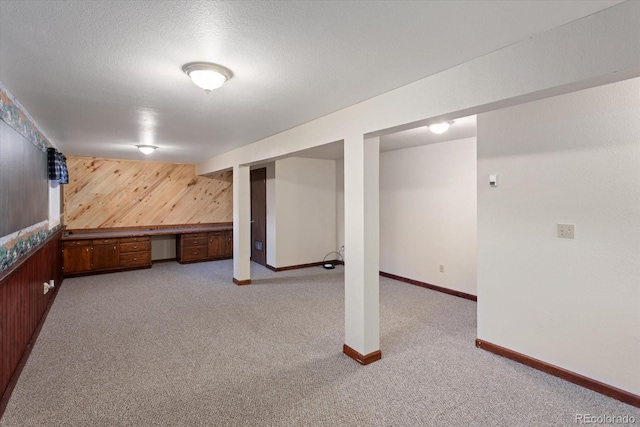 basement featuring wooden walls, light carpet, and a textured ceiling