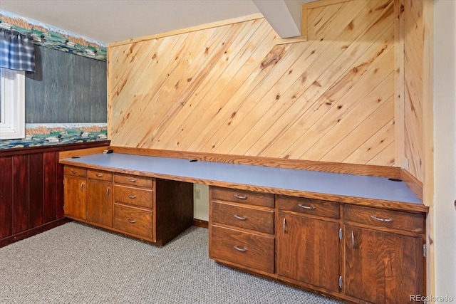 unfurnished office with wood walls, light colored carpet, and built in desk