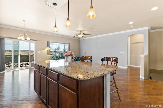 kitchen with a kitchen island, dark wood-type flooring, pendant lighting, a breakfast bar, and arched walkways