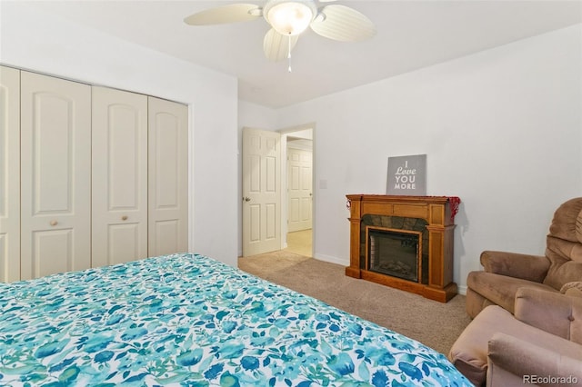 carpeted bedroom featuring a glass covered fireplace, baseboards, a closet, and ceiling fan