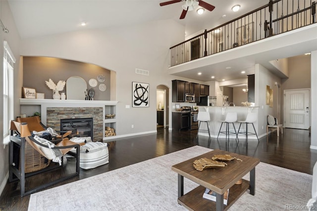living room featuring a ceiling fan, baseboards, dark wood-type flooring, a fireplace, and high vaulted ceiling