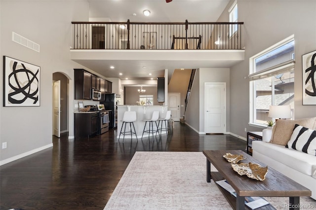 living area featuring a high ceiling, dark wood-type flooring, healthy amount of natural light, arched walkways, and baseboards