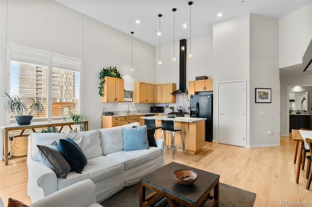 living room with a high ceiling, sink, and light hardwood / wood-style floors