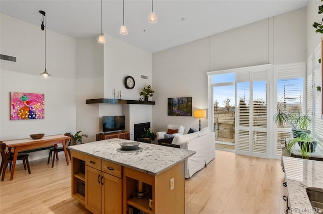 kitchen featuring a high ceiling, light hardwood / wood-style floors, light stone counters, and pendant lighting