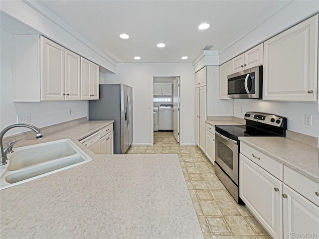 kitchen featuring washer and dryer, sink, white cabinets, and stainless steel appliances