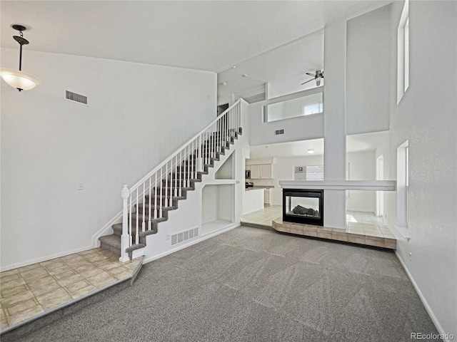 unfurnished living room featuring carpet, ceiling fan, a towering ceiling, and a tiled fireplace