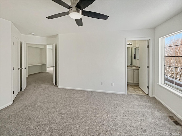 unfurnished bedroom featuring ceiling fan, light colored carpet, connected bathroom, and multiple windows