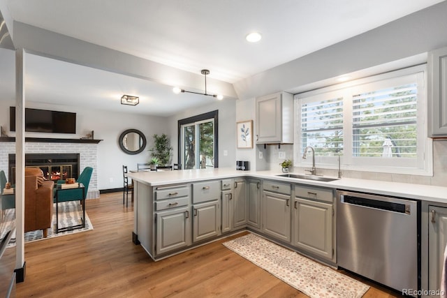 kitchen featuring a peninsula, a fireplace, gray cabinets, a sink, and stainless steel dishwasher