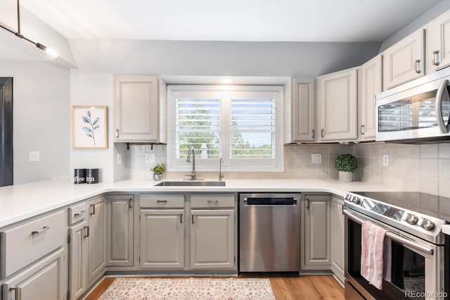 kitchen featuring a sink, decorative backsplash, light countertops, stainless steel appliances, and light wood-style floors