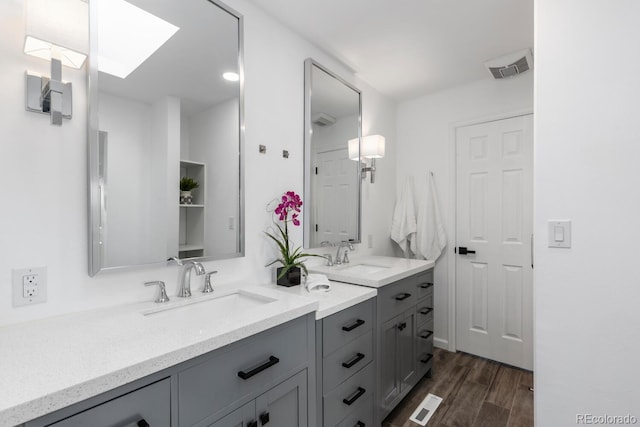 bathroom with a sink, visible vents, wood finished floors, and double vanity