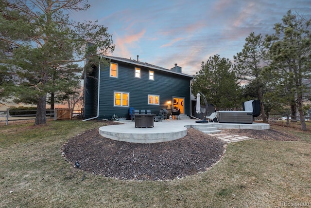 back of house at dusk featuring a patio area, a lawn, a chimney, and a hot tub